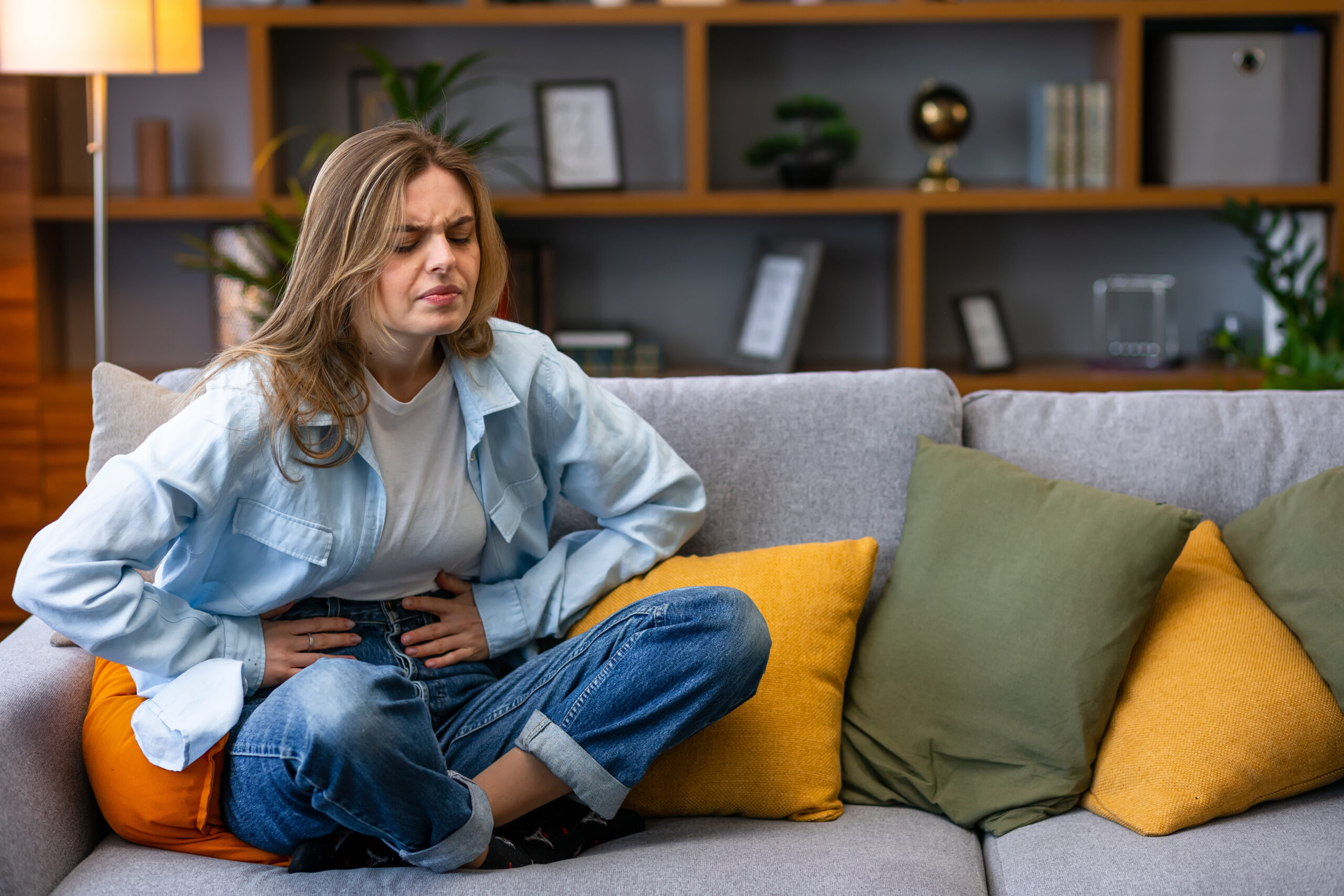 Portrait of woman with stomach ache sitting sofa and holding hands on her stomach.